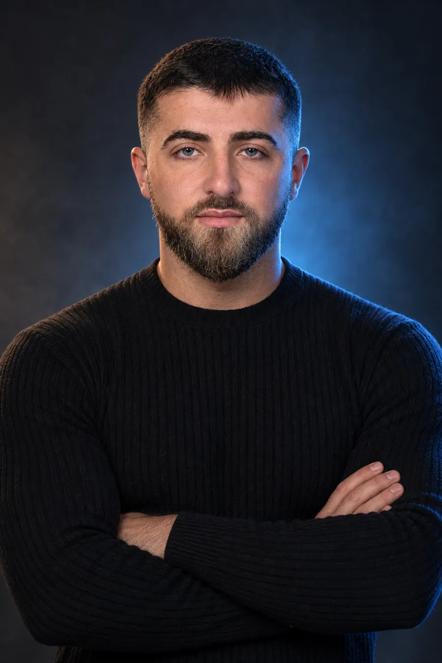 Adam Mustapaev mit verschränkten Armen im dunklen Studio mit eisblauem Licht